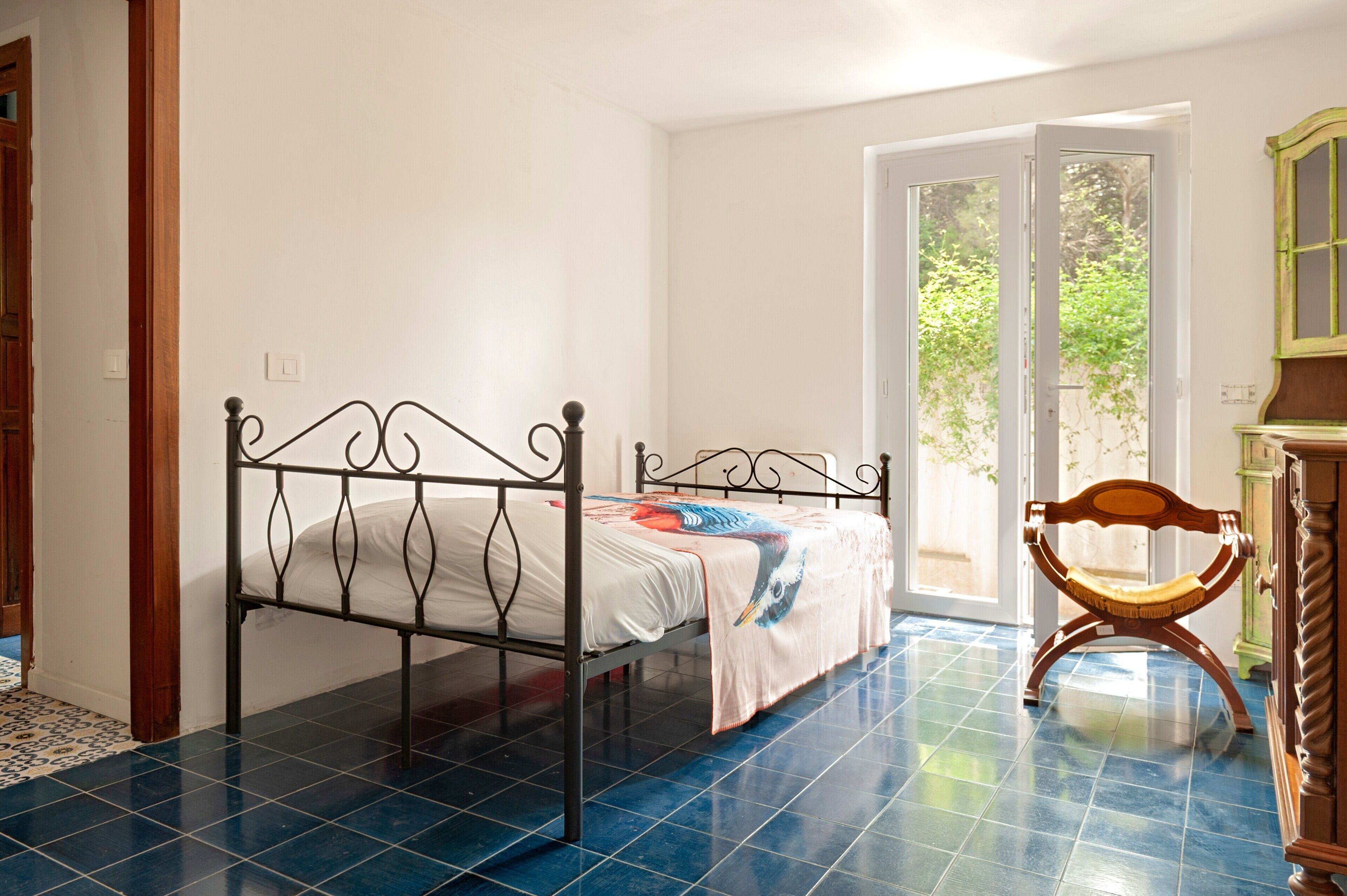 Ein Schlafzimmer mit einem Metallbettgestell, einem hölzernen Stuhl und einer Tür, die auf einen Balkon führt.