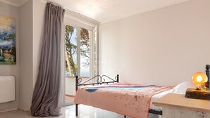 A bedroom with a bed, a window, a radiator, and a painting on the wall. - Villa 'Magnolie' with Sea View, Private Garden and Air Conditioning (Chioma)