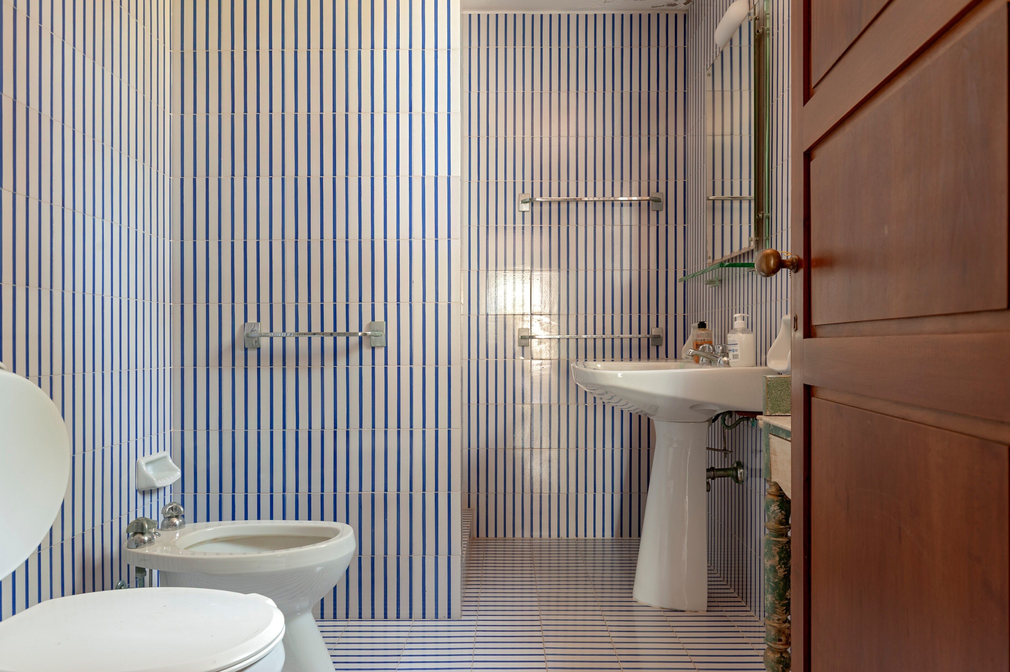 A bathroom with striped tile walls, a sink, a toilet, and a shower area.