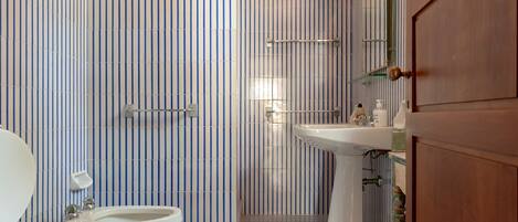 A bathroom with striped tile walls, a sink, a toilet, and a shower area.