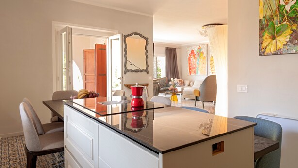 A modern kitchen with a glass-top island, a red kettle, and a dining area with chairs and a table. - Villa 'Magnolie' with Sea View, Private Garden and Air Conditioning (Chioma)