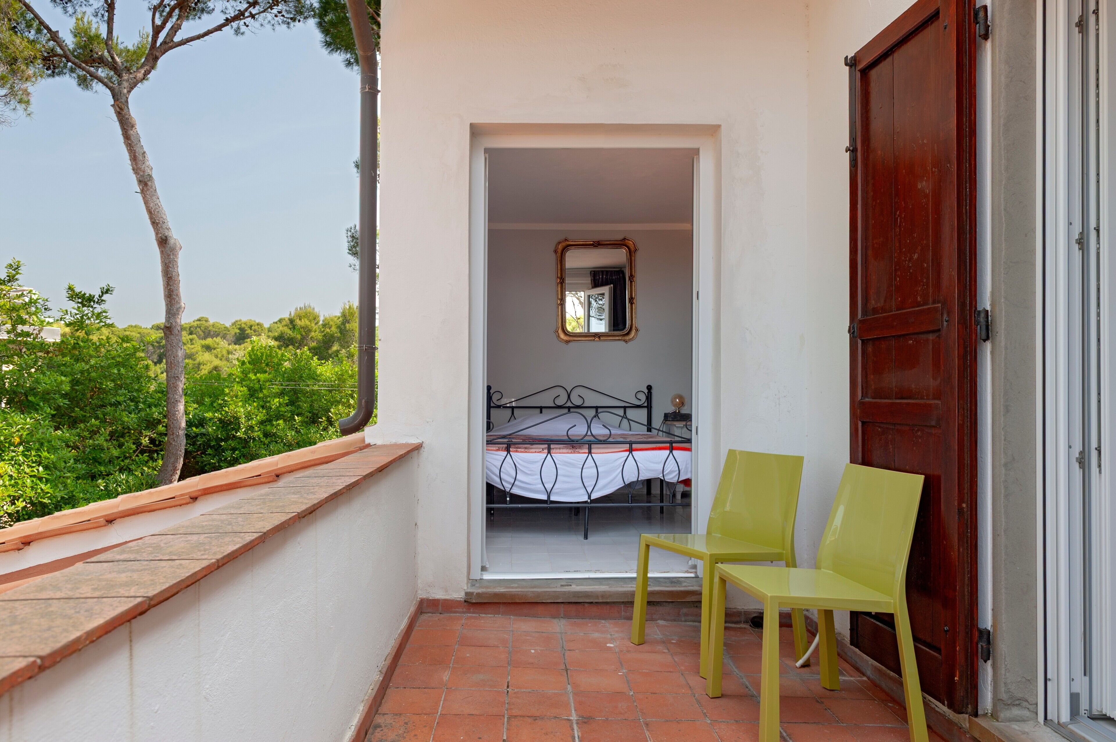 A balcony with a bed, a mirror, and two chairs.