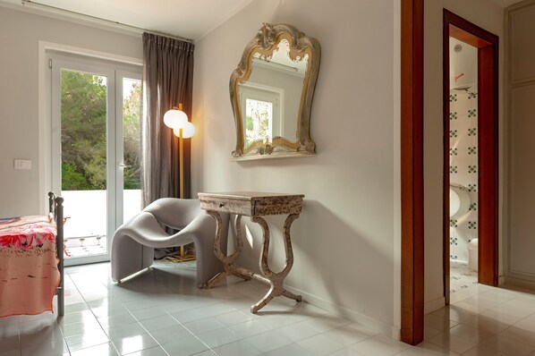 Une pièce comprenant un lit, une chaise, une table, un miroir et une porte donnant sur une salle de bain.