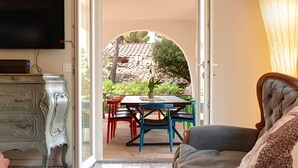 An open doorway leading to a patio with a table and chairs, a television on the wall, and a sofa inside. - Villa 'Magnolie' with Sea View, Private Garden and Air Conditioning (Chioma)