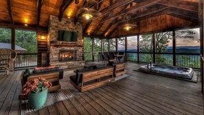 A spacious outdoor deck with a stone fireplace, seating area, and a hot tub. - Ridge Top Lodge - Incredible Mtn Views | Hot Tub | Game Room | Outdoor Fireplace (Blue Ridge)