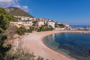 Une ville côtière dotée d’une plage de sable, d’eaux bleues et limpides, et de bâtiments construits sur une colline.