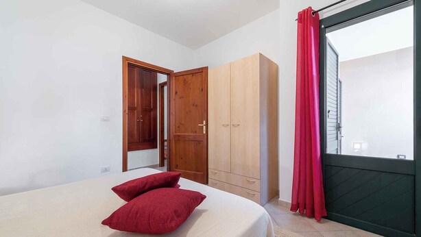 A bedroom with a bed, red pillows, a wardrobe, and a sliding door to a balcony.