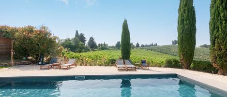 A swimming pool with lounge chairs and tall cypress trees.