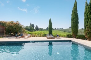 A swimming pool with lounge chairs and tall cypress trees.