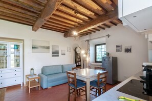 A kitchen with a dining table, chairs, a blue sofa, a wooden ceiling, and a refrigerator.