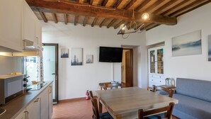 Een keuken met houten balken, een eettafel met stoelen, een aan de muur gemonteerde televisie en een bank.