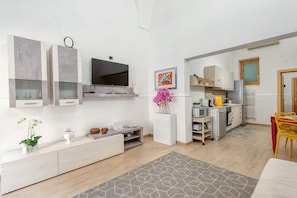 Un soggiorno moderno con una TV a schermo piatto, un'area pranzo con una sedia gialla e una cucina con un forno a microonde.