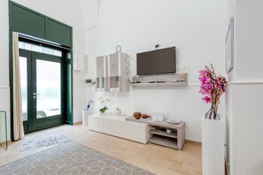 Un salon moderne avec un téléviseur, des meubles blancs, une console et une porte donnant sur une vue agréable.