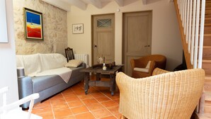 A living room with a sofa, a wicker chair, a small table, and a painting on the wall. - La Grange d'Oustaud with Pool, Countryside Views, and Authentic Charm (Unknown)