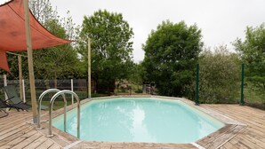 A swimming pool with a wooden deck, metal pool ladder, and a red canopy. - La Grange d'Oustaud with Pool, Countryside Views, and Authentic Charm (Unknown)
