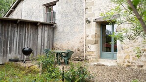 A stone building with a wooden fence, a barbecue grill, and a table with chairs. - La Grange d'Oustaud with Pool, Countryside Views, and Authentic Charm (Unknown)