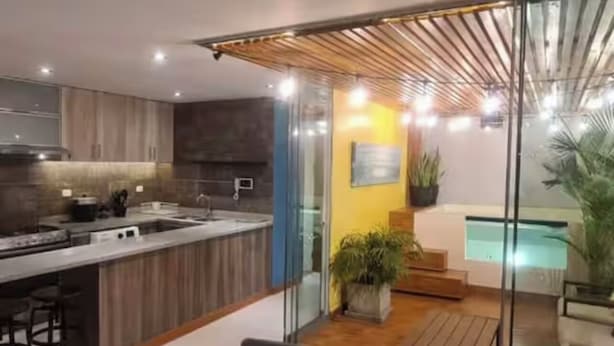 A modern kitchen with a central island, a dining area with a glass table and chairs, and a view of a swimming pool through a glass door. - Delightful 1, 2 o 3 bedroom apartment in Ica (Ica)