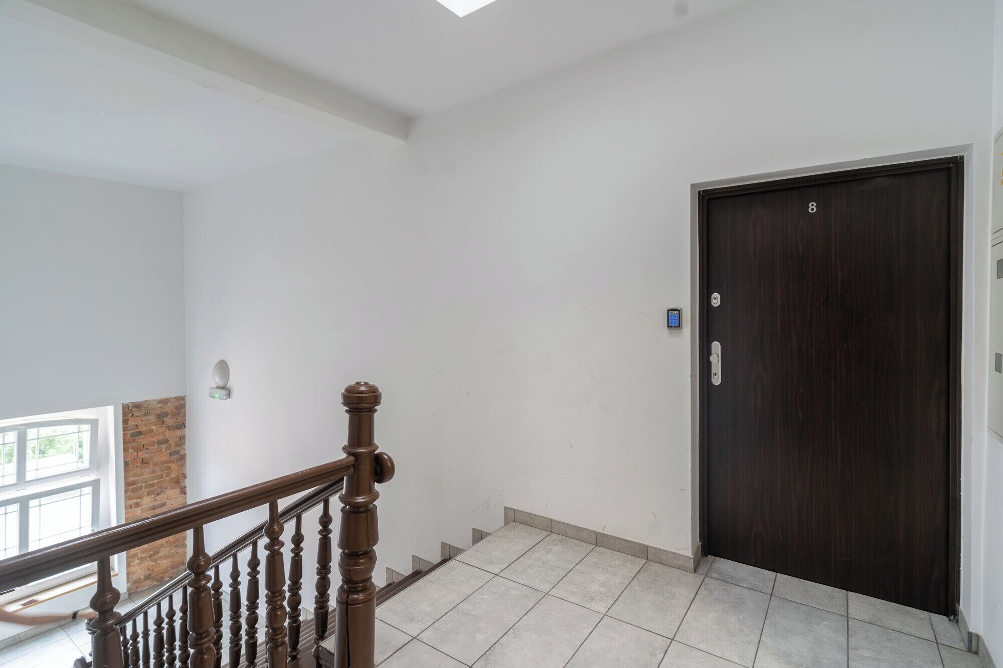 Una scala con ringhiera in legno che conduce a una porta scura in legno dotata di serratura a codice.