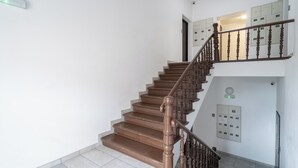 Un escalier avec des marches en bois et une rampe en bois, menant à un palier où se trouvent un interrupteur et un tableau électrique fixé au mur.