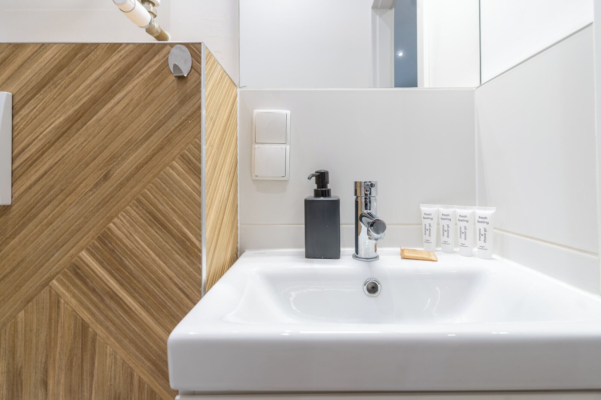 Ein modernes Badezimmer mit einem weißen Waschbecken, einem schwarzen Seifenspender und vier Flaschen Shampoo und Conditioner.