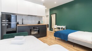 Une chambre d’hôtel moderne avec une kitchenette, un lit recouvert d’une couverture bleue et un mur d’accent vert.