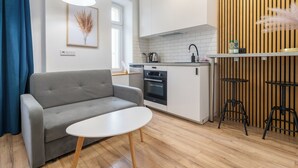 A modern living room with a grey sofa, a white coffee table, and a kitchen area with white cabinets, a stove, and a sink.
