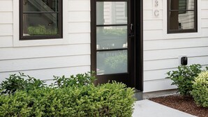 A white building with a black-framed front door, two black awnings, and a small window with a number plate.