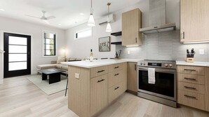 Una cocina moderna con armarios de madera clara, una isla central, electrodomésticos de acero inoxidable e iluminación colgante.