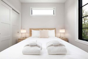A hotel room with a large bed, two bedside tables with lamps, a window with a view, and a door on the left. - Hamilton Place | Dunecrest Building | 5 Units (Traverse City)