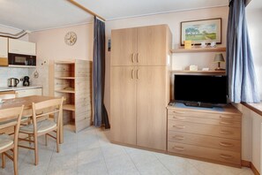 A compact room with a wooden dining table, chairs, a TV, a microwave, a coffee maker, and a cabinet with drawers. - Apartment 'Loredana 1' with Mountain View, Shared Garden and Wi-Fi (Livigno)