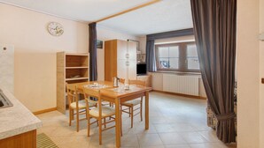 Una cocina compacta con comedor, una estantería empotrada y un ventanal con cortinas.