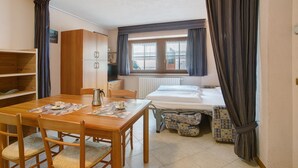 Un dormitorio con cama, ventana, radiador, mesa de madera con sillas y armario.