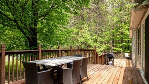 A wooden deck with a table and chairs, surrounded by dense trees. - Maple City Farm | Pet Friendly (Maple City)