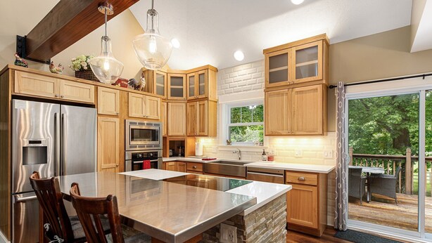 A modern kitchen with wooden cabinets, a large island, stainless steel appliances, and a view to the outdoors. - Maple City Farm | Pet Friendly (Maple City)