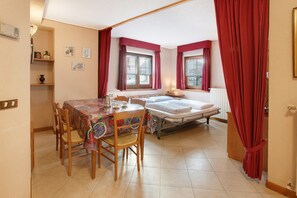 Un dormitorio con cama, una mesa con sillas, una ventana con cortinas y un radiador.