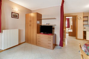 Una habitación con un armario de madera, un televisor de pantalla plana, un radiador y un reloj en la pared.