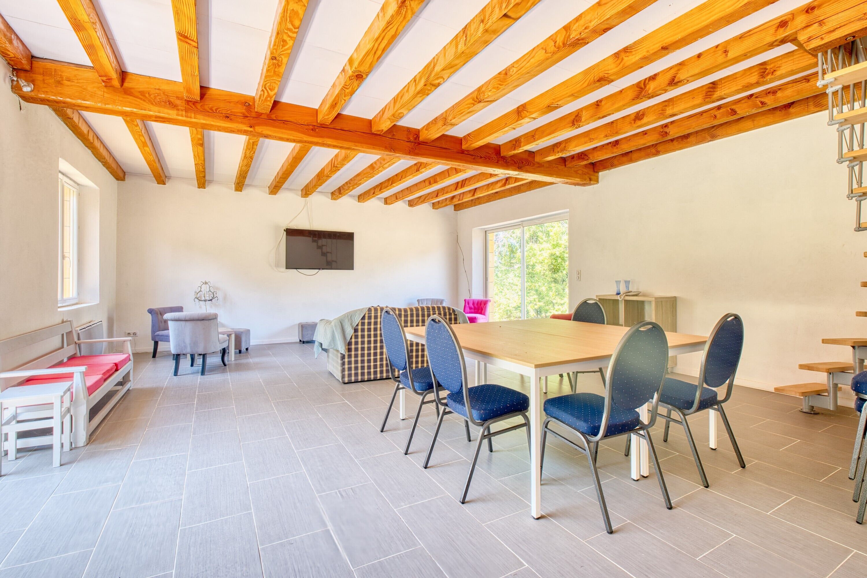 Een ruime kamer met een houten plafond, een eettafel met stoelen, een bank en een televisie aan de muur.