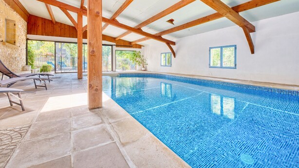 An indoor swimming pool with stone flooring, wooden beams, and a stone wall.