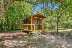 Una cabaña de madera amarilla con un porche, rodeada de árboles en un bosque.