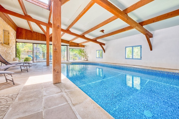 An indoor swimming pool with stone flooring, wooden beams, and a stone wall.