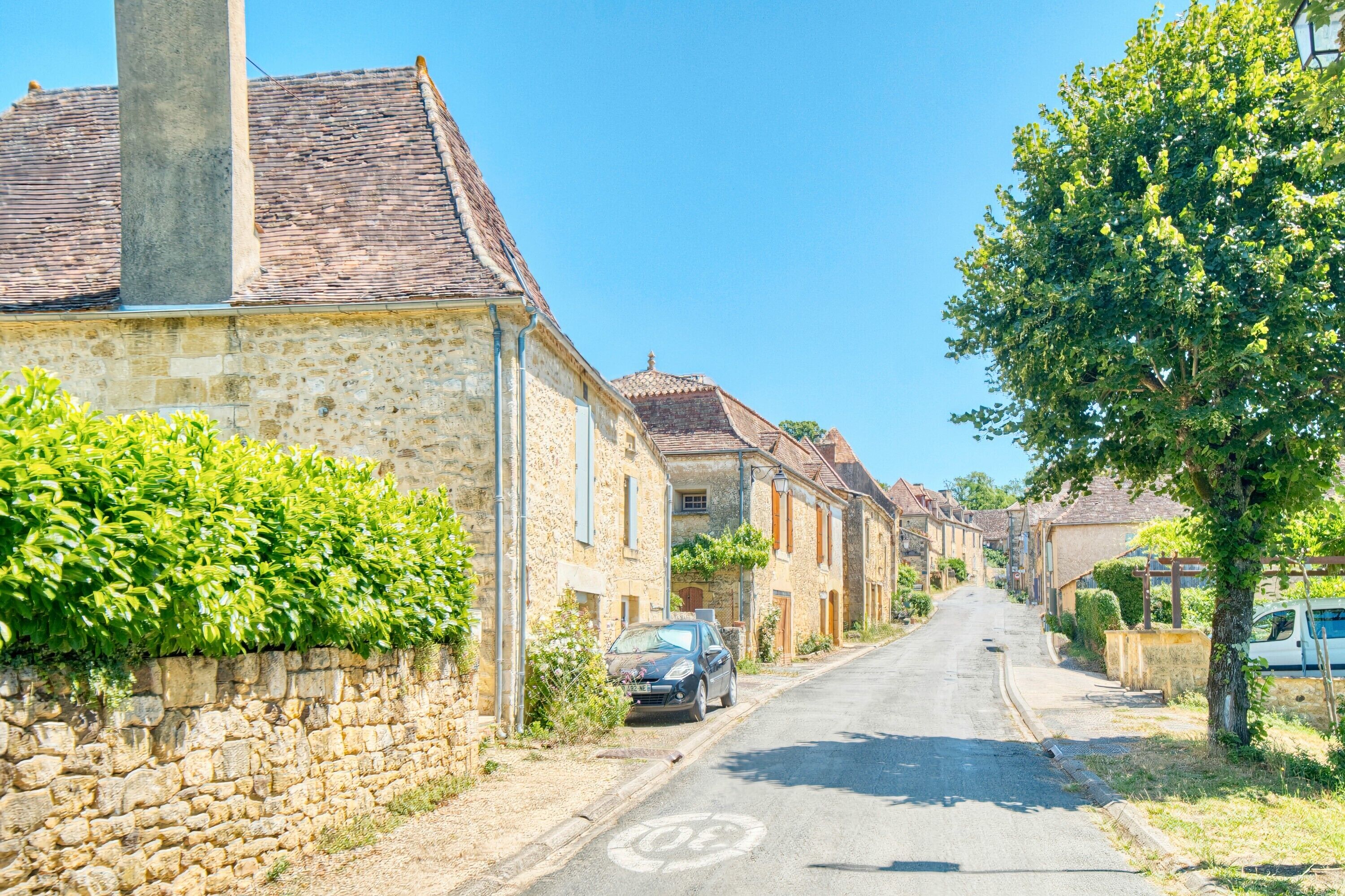 A narrow street lined with stone buildings, a parked car, and a tree on the right.