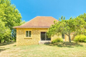 A stone house with a tiled roof, a small porch, and a lawn.