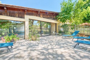 A covered patio with a stone floor, glass doors, and blue lounge chairs.
