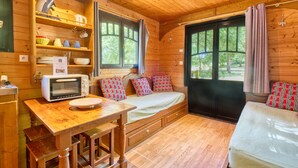 Interior de una cabaña de madera con kitchenette, una cama y ventana con vistas a un bosque.