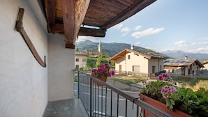 Un balcone con ringhiera metallica, piante in vaso e vista su un paesaggio montano.
