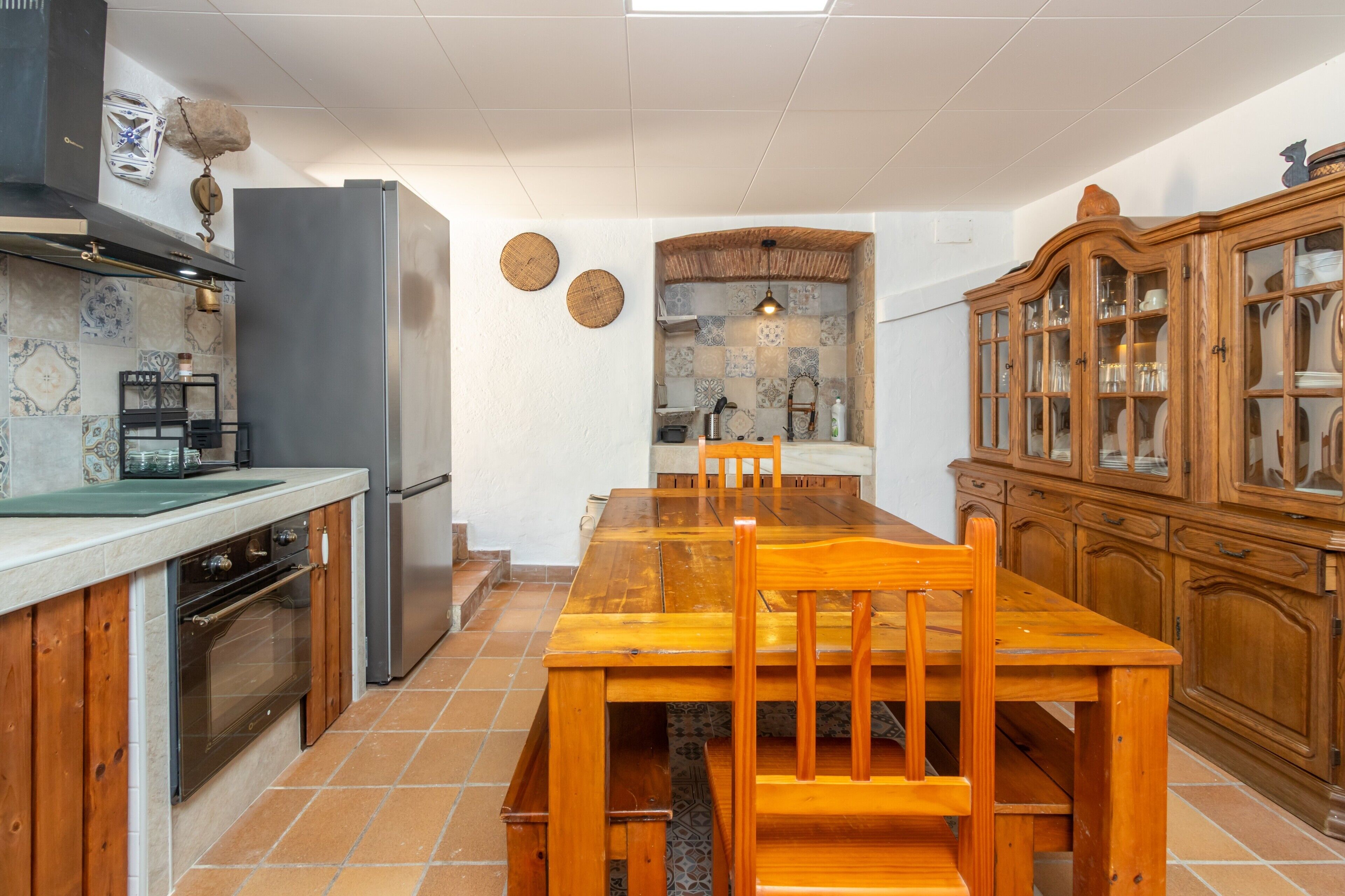 A kitchen with a wooden table, chairs, a refrigerator, and a cabinet.