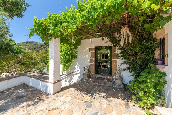 A stone-paved courtyard with a white building, green shutters, and a statue.