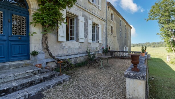 A stone building with a blue door, white shutters, and a gravel courtyard.