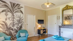 A room with a large tropical mural, a television, a fireplace, and a bed with blue towels.