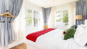 A bedroom with a large bed, a wooden hanger, and a view of the outdoors through large windows. - Herons Perch: Peaceful Lakefront Cottage in Shipshewana close to all the fun! (Shipshewana)